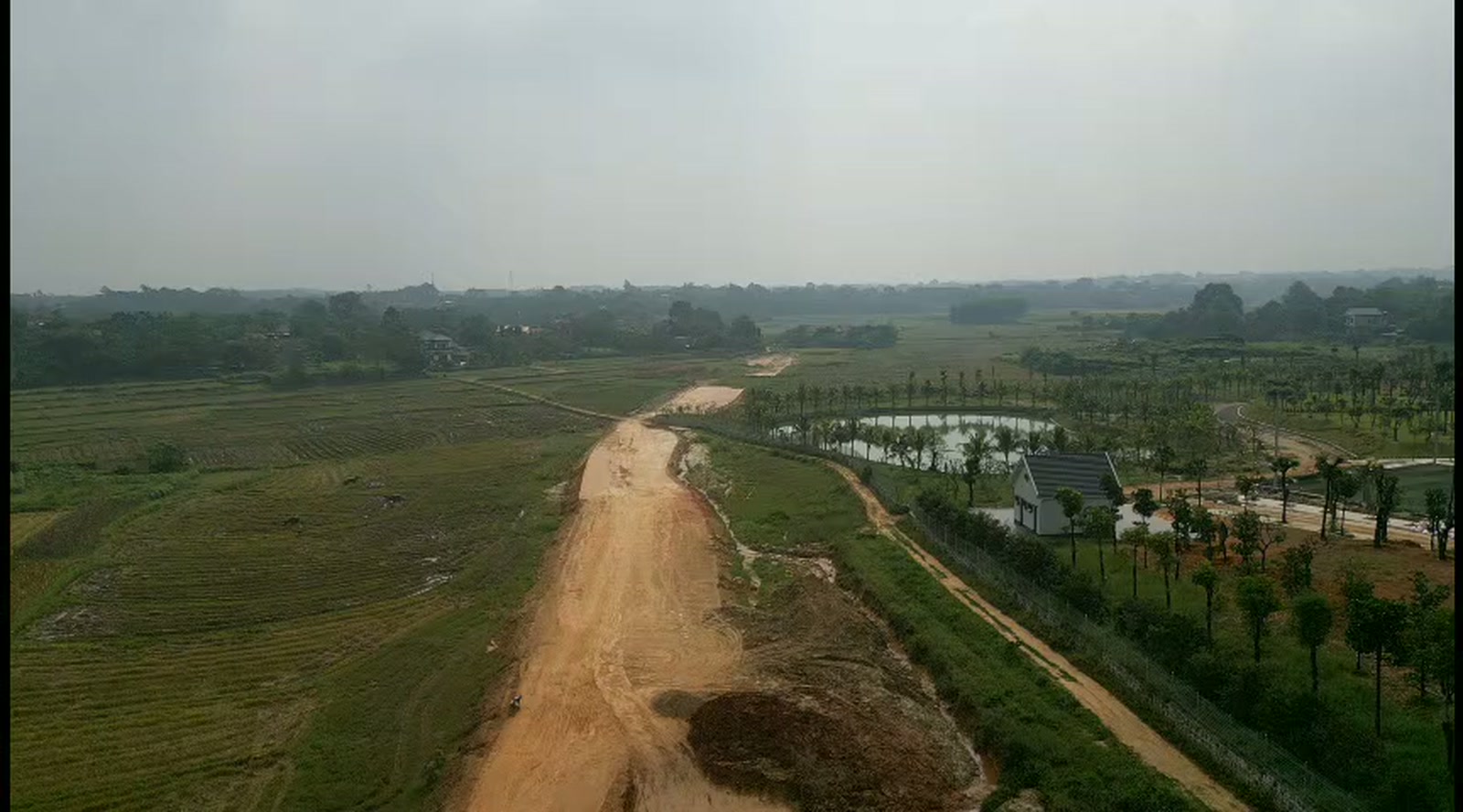 Đường đang mở cạnh ruộng — phần đất chưa san nền của giai đoạn sau.